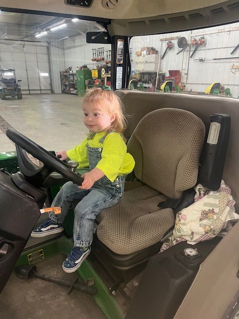 A little girl is sitting in the driver 's seat of a tractor.