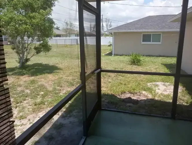 Screened porch overlooking a grassy yard, with a house and fence in the background.