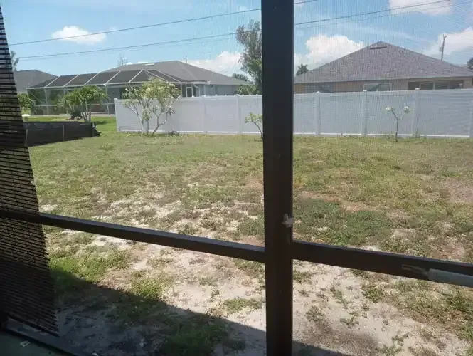 View from a screened porch of a grassy backyard with a white fence and houses.