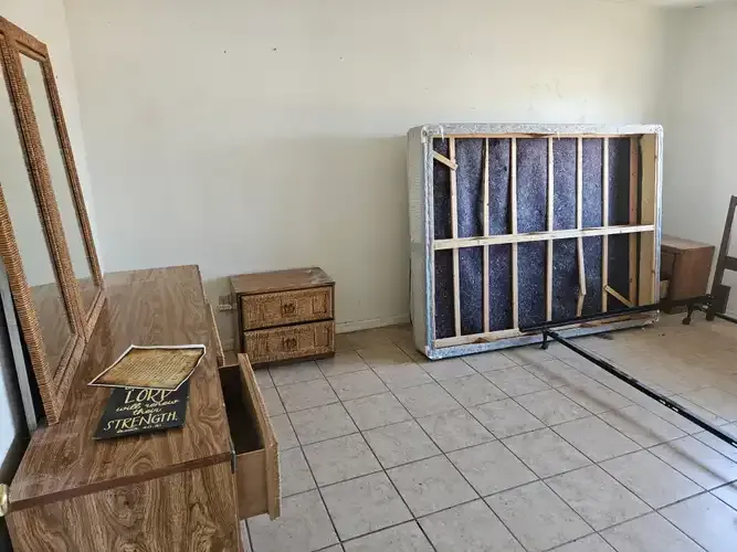 Bedroom with dresser, nightstand, exposed bed frame, and tiled floor.