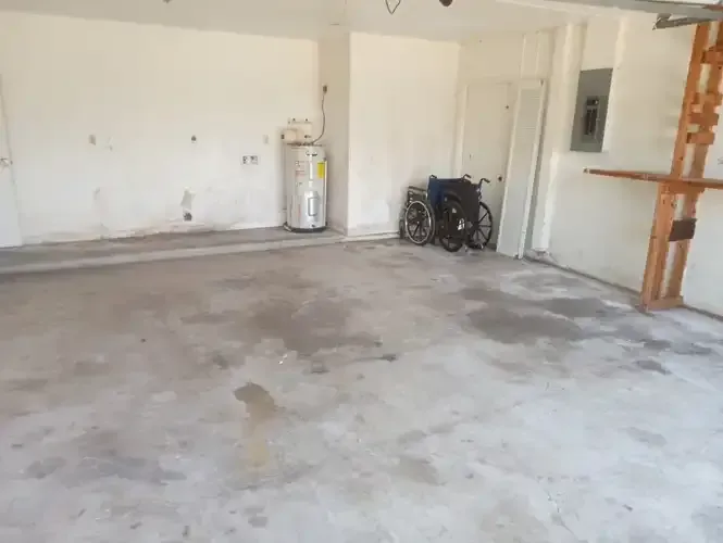 Empty garage with concrete floor, water heater, and a wheelchair.