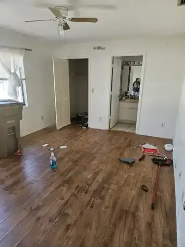 A cluttered bedroom with brown wood-look flooring, open closet, and attached bathroom.