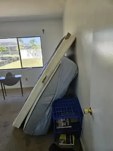 Mattress, headboard, and blue pet carrier leaning against a wall in a room with a window and a door.