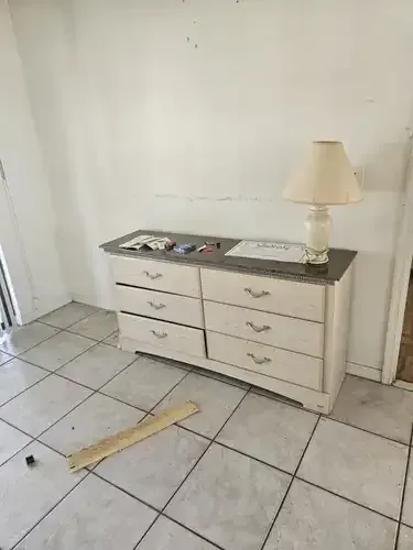 A dresser with a lamp on top, in a room with tiled floor and white walls.