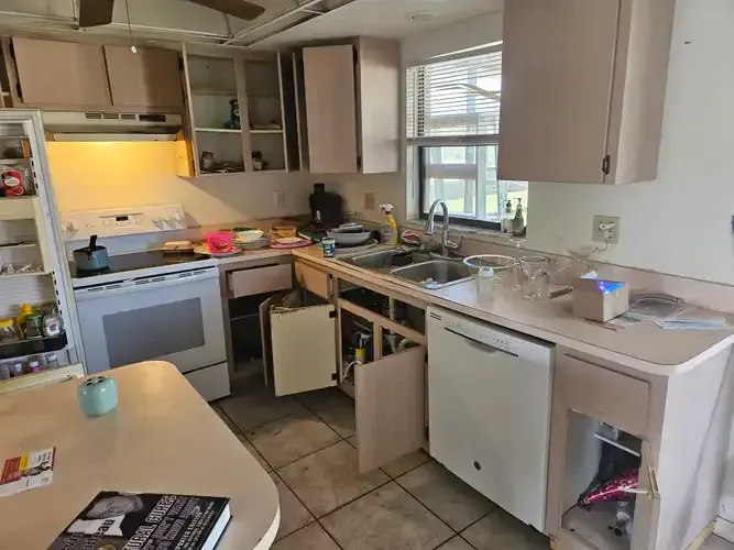 Kitchen undergoing renovation: cabinets open, appliances visible, countertop and table cluttered.