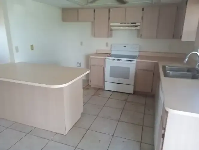 Empty kitchen with pink cabinets, white appliances, and a central island.