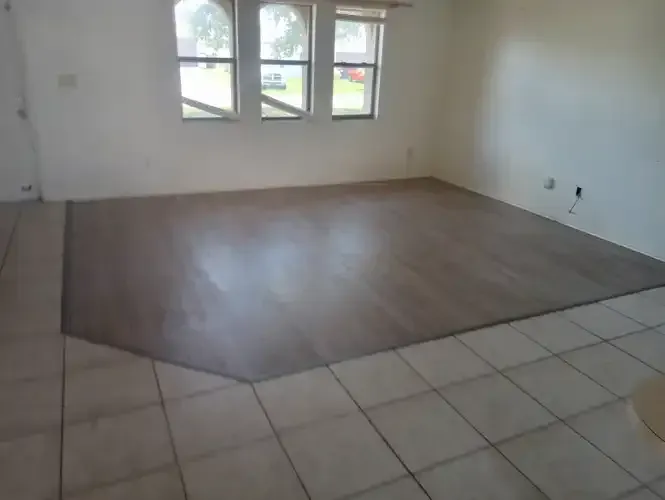 Room with tile floor transitioning to a raised, wooden floor area. Windows are in the background.