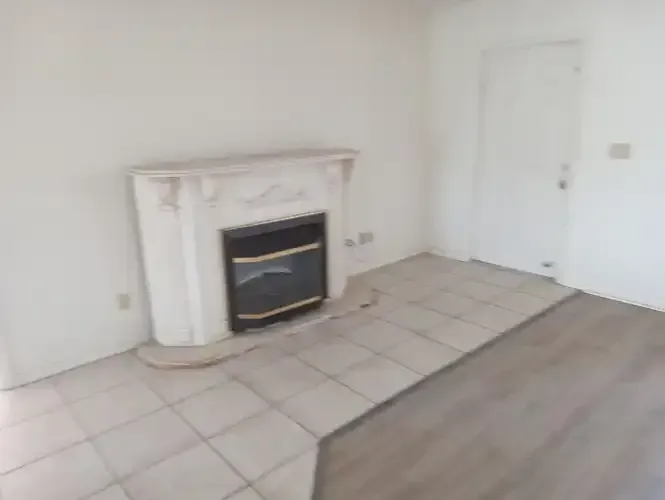 Empty room with white fireplace, tile floor, and a door on the right.