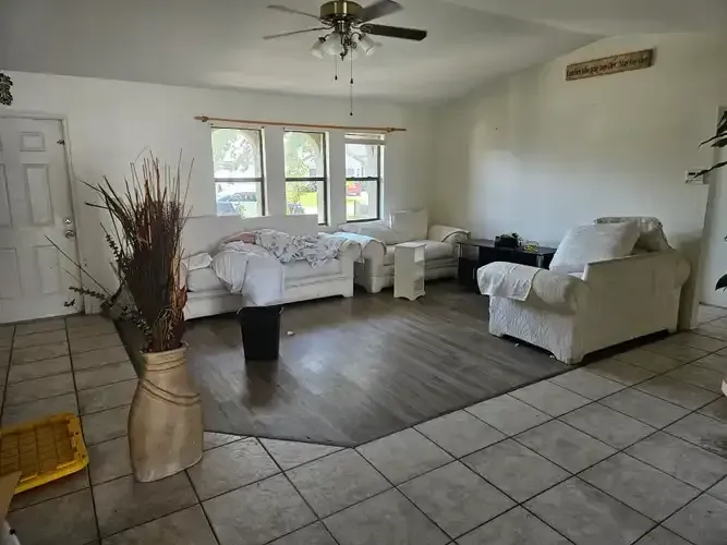 Living room with white sofas, chairs, vase of dried plants, and tile/wood floors.
