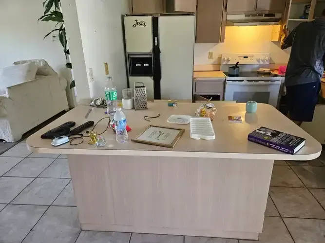 Kitchen island with items on top, fridge in background, person near stove.