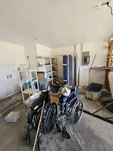Two wheelchairs in a cluttered garage, with shelving and storage.