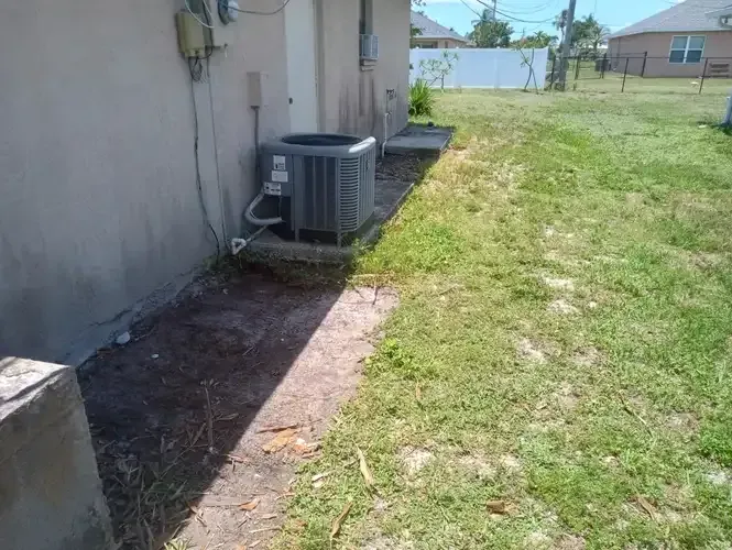 AC unit next to house, bordering a grassy area and a fence.