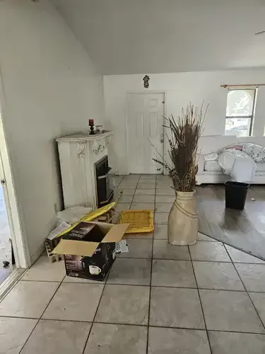 Living room with white walls, tiled floor, a decorative fireplace, and a large vase of dried plants.