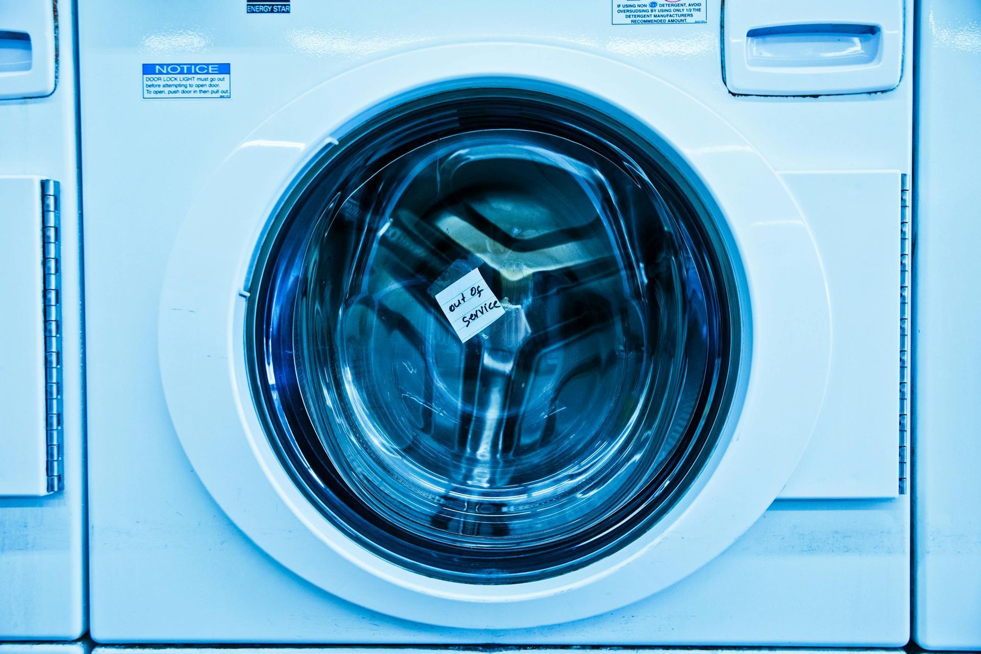 A front-load washing machine, blue-tinted, door closed, in a laundromat.