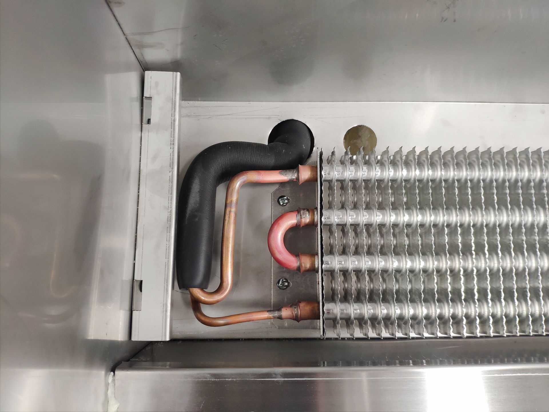 Copper pipes and cooling fins inside a silver refrigerator.