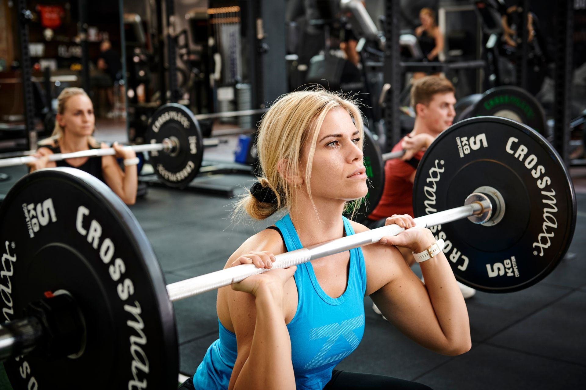 Tre kvinder løfter vægte over hovedet i et fitnesscenter.