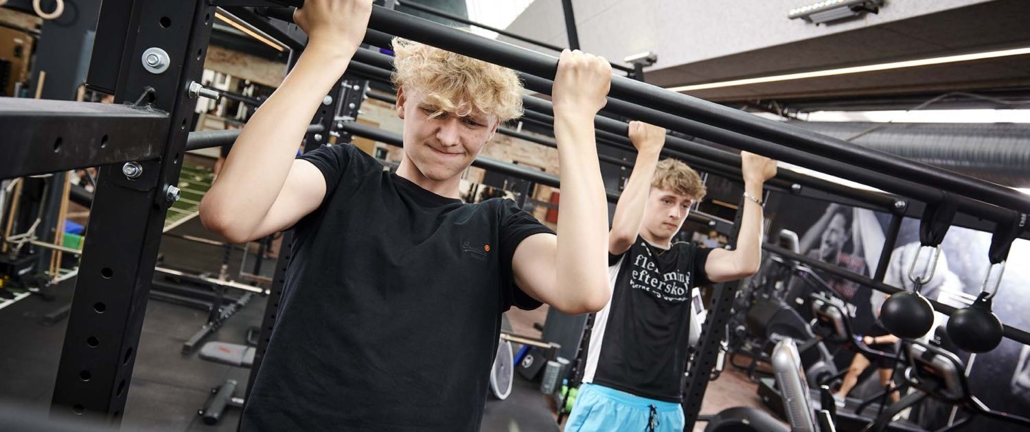 En mand laver pull ups på en bar i et fitnesscenter.
