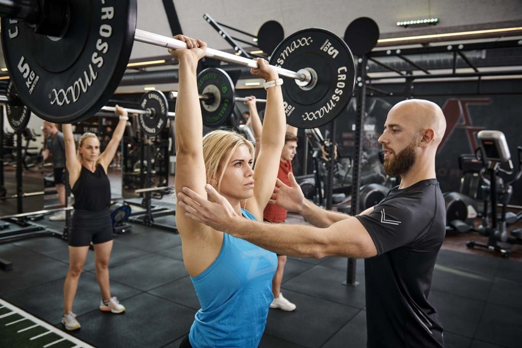 En mand hjælper en kvinde med at løfte en vægtstang i et fitnesscenter.