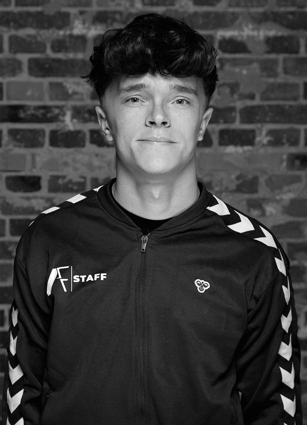 Et sort/hvidt foto af en ung mand, der står foran en murstensvæg.