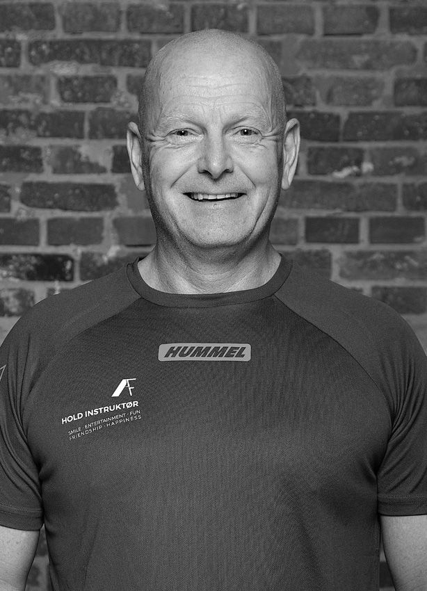 En skaldet mand smiler foran en murstensvæg på et sort-hvidt foto.