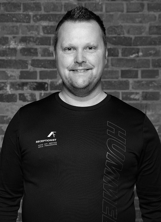 En mand i en sort skjorte smiler i et fitnesscenter.