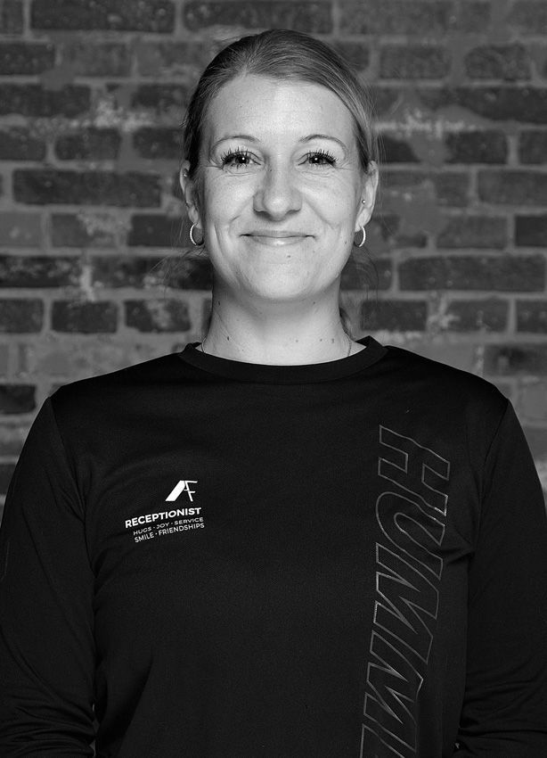 En kvinde i en sort skjorte smiler foran en murstensvæg.