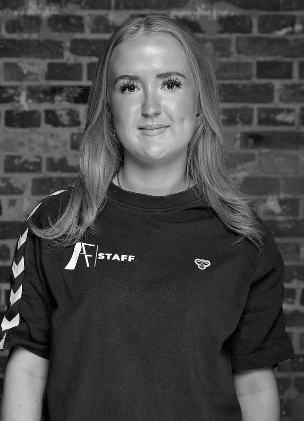 Et sort/hvidt foto af en kvinde iført en t-shirt foran en murstensvæg.