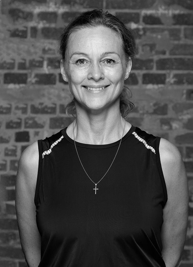 En kvinde iført en sort tanktop og en kryds halskæde smiler på et sort/hvidt foto.