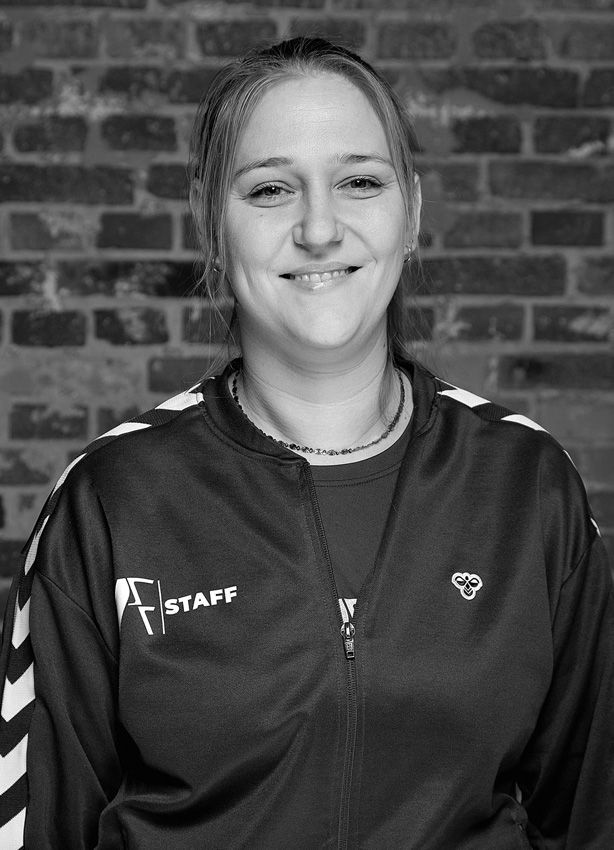 En kvinde på et sort/hvidt foto smiler foran en murstensvæg.