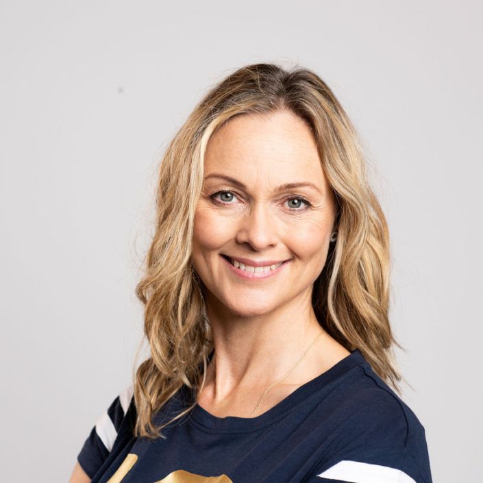 En kvinde i en blå skjorte smiler til kameraet