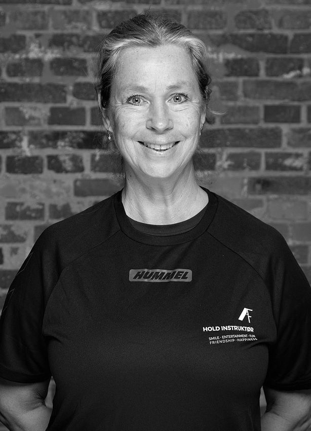 En kvinde i sort skjorte og halskæde smiler i et fitnesscenter.