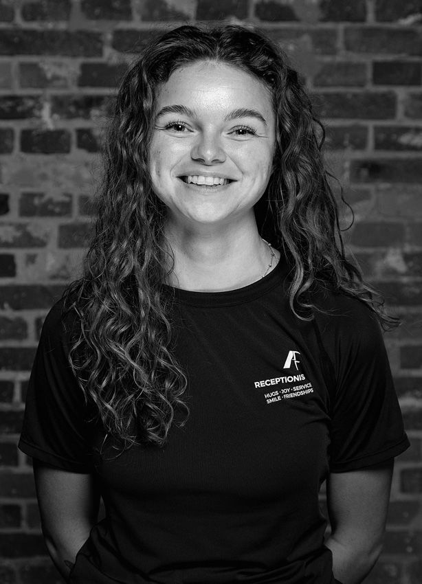 Et sort/hvidt foto af en kvinde smilende foran en murstensvæg.