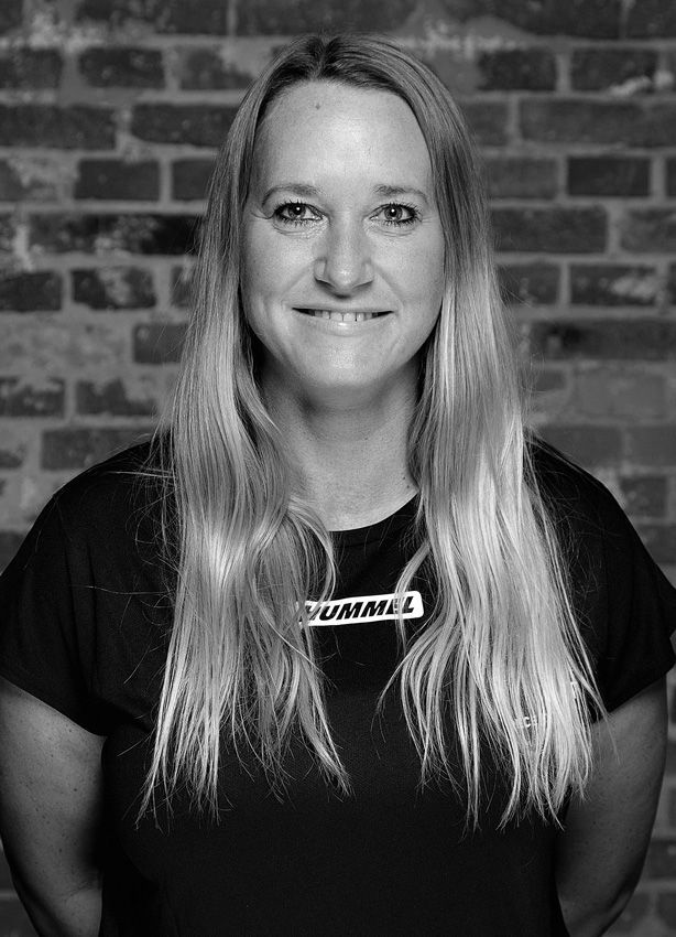 En kvinde smiler foran en murstensvæg på et sort-hvidt foto.