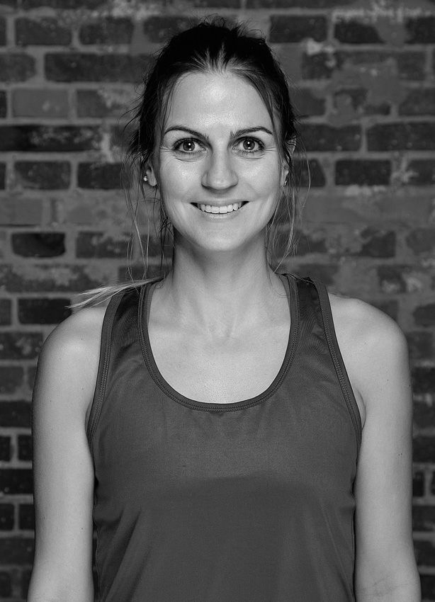 En kvinde i en tanktop smiler foran en murstensvæg.