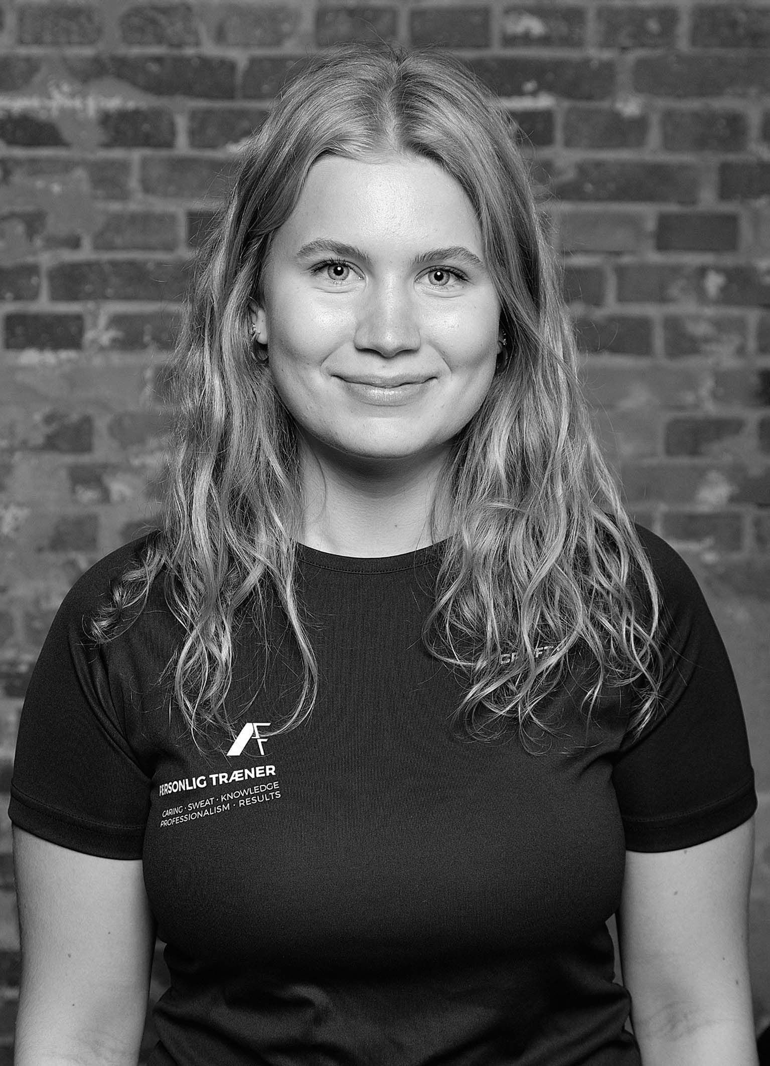 En kvinde i en sort skjorte smiler i et fitnesscenter.