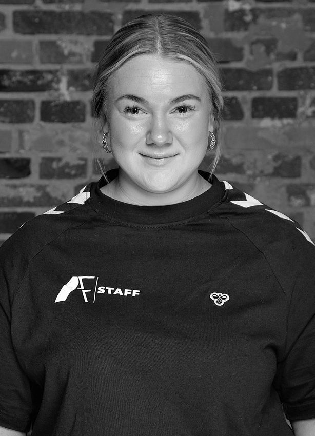 En kvinde iført en sort skjorte med ordet staff på smiler på et sort/hvidt foto.