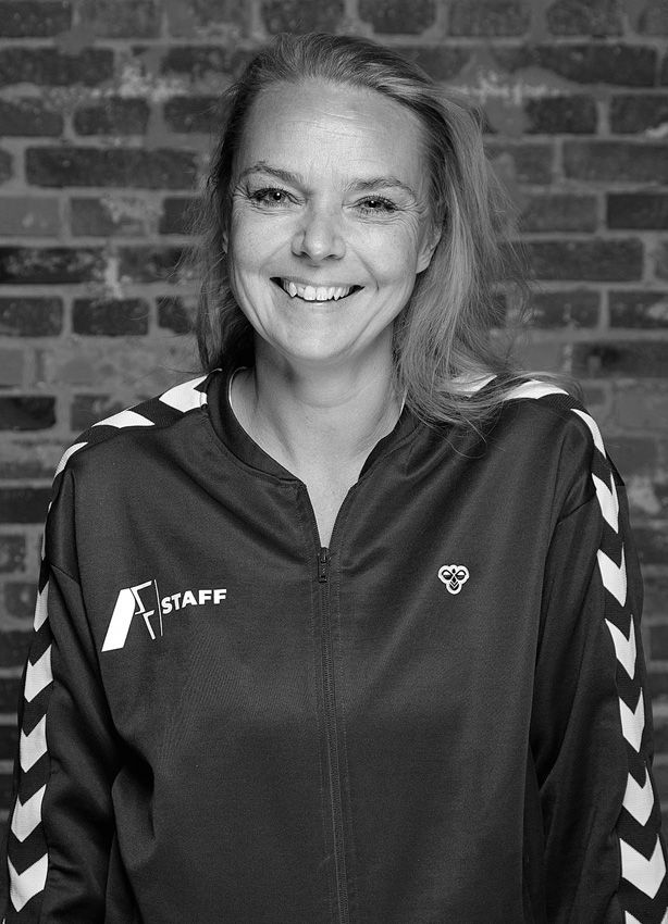 En kvinde på et sort/hvidt foto smiler foran en murstensvæg.