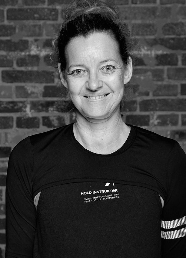 En kvinde står i et fitnesscenter iført en grøn sweater og en halskæde.