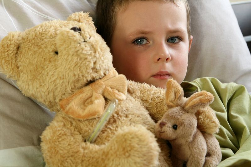 Boy in bed with a teddy bear and small stuffed rabbit, looking sad and ill.