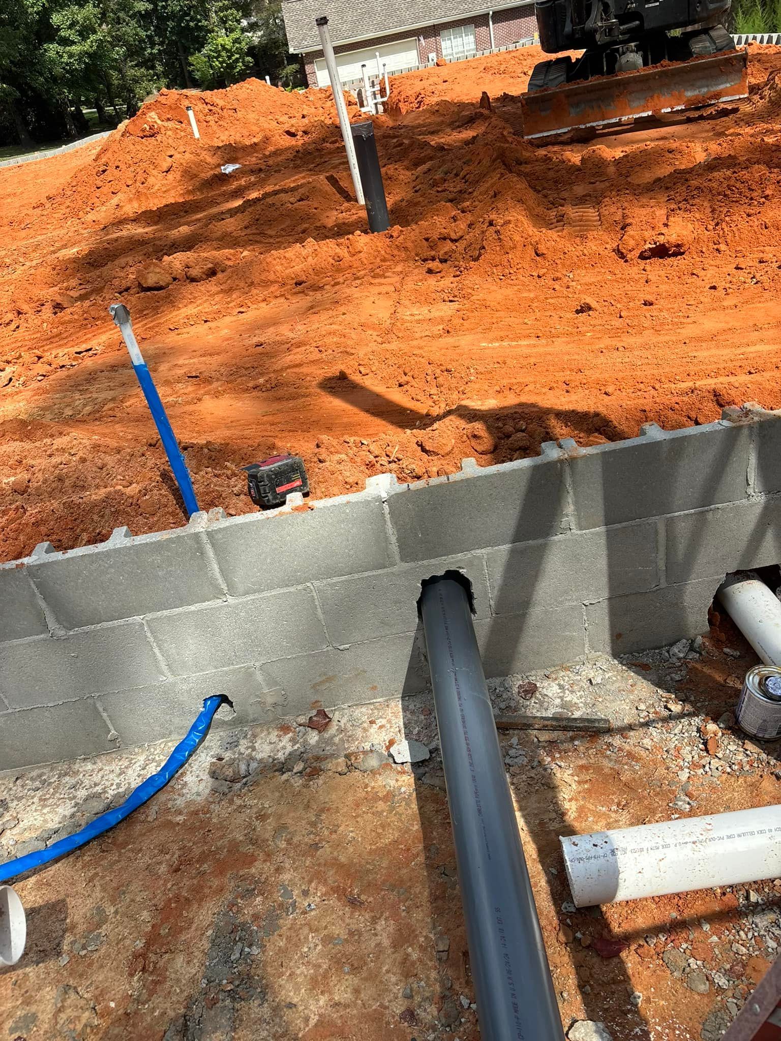 A pipe is being installed in the ground next to a brick wall.