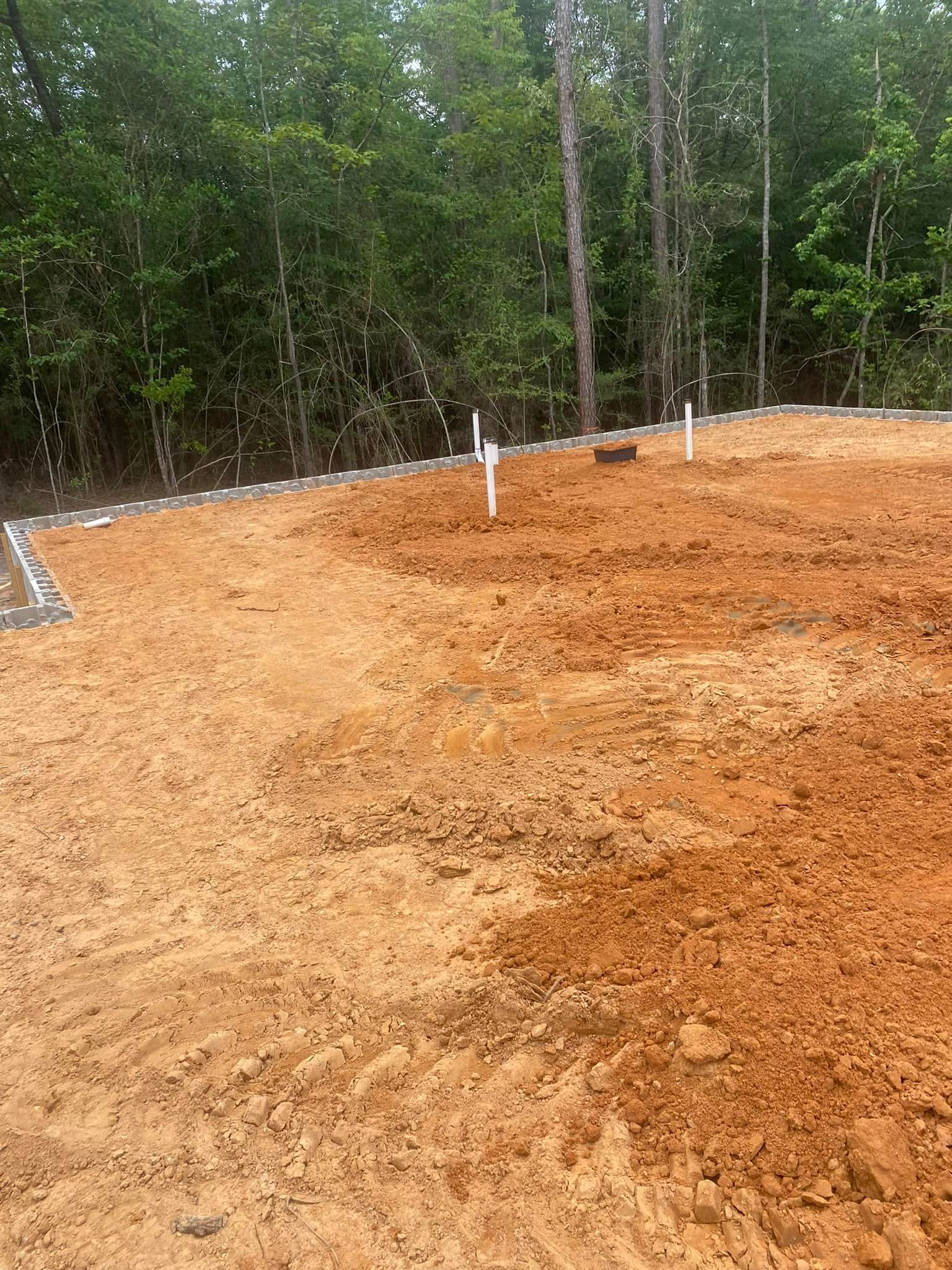 A dirt field with a fence and trees in the background.