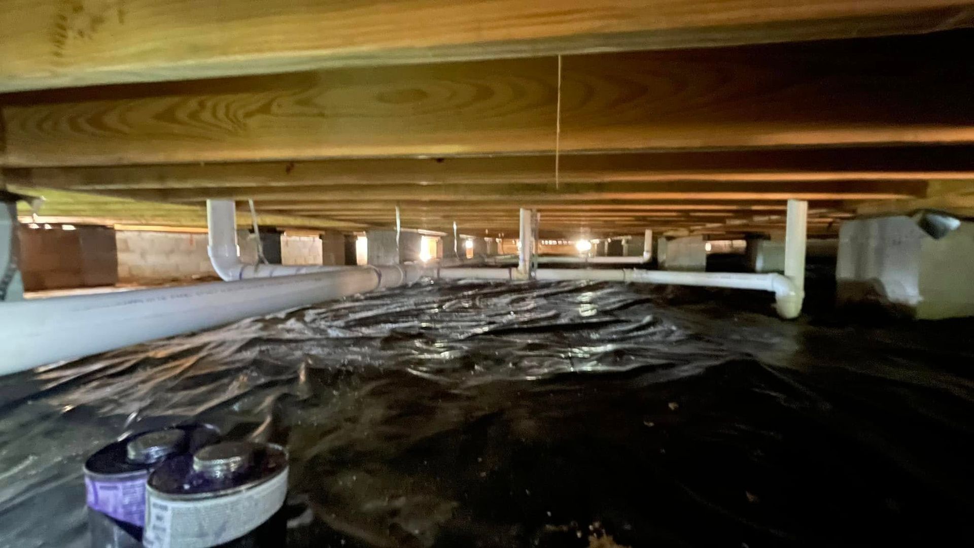 A crawl space under a house with a lot of pipes.