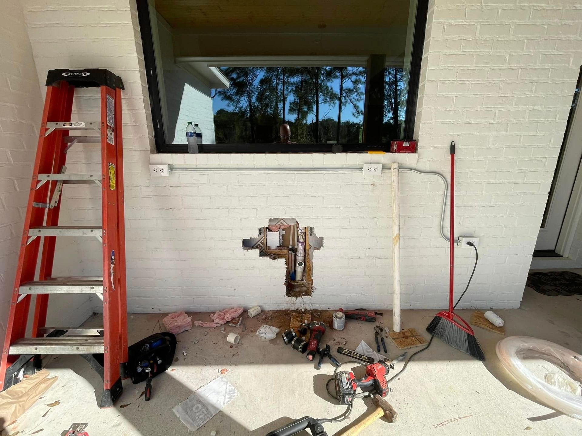 A ladder is sitting on the ground in front of a white brick wall.