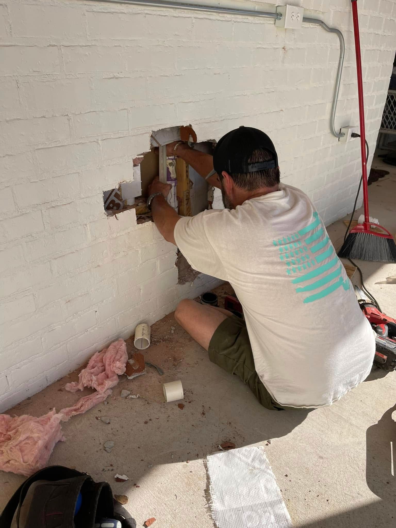 A man is sitting on the ground working on a wall.