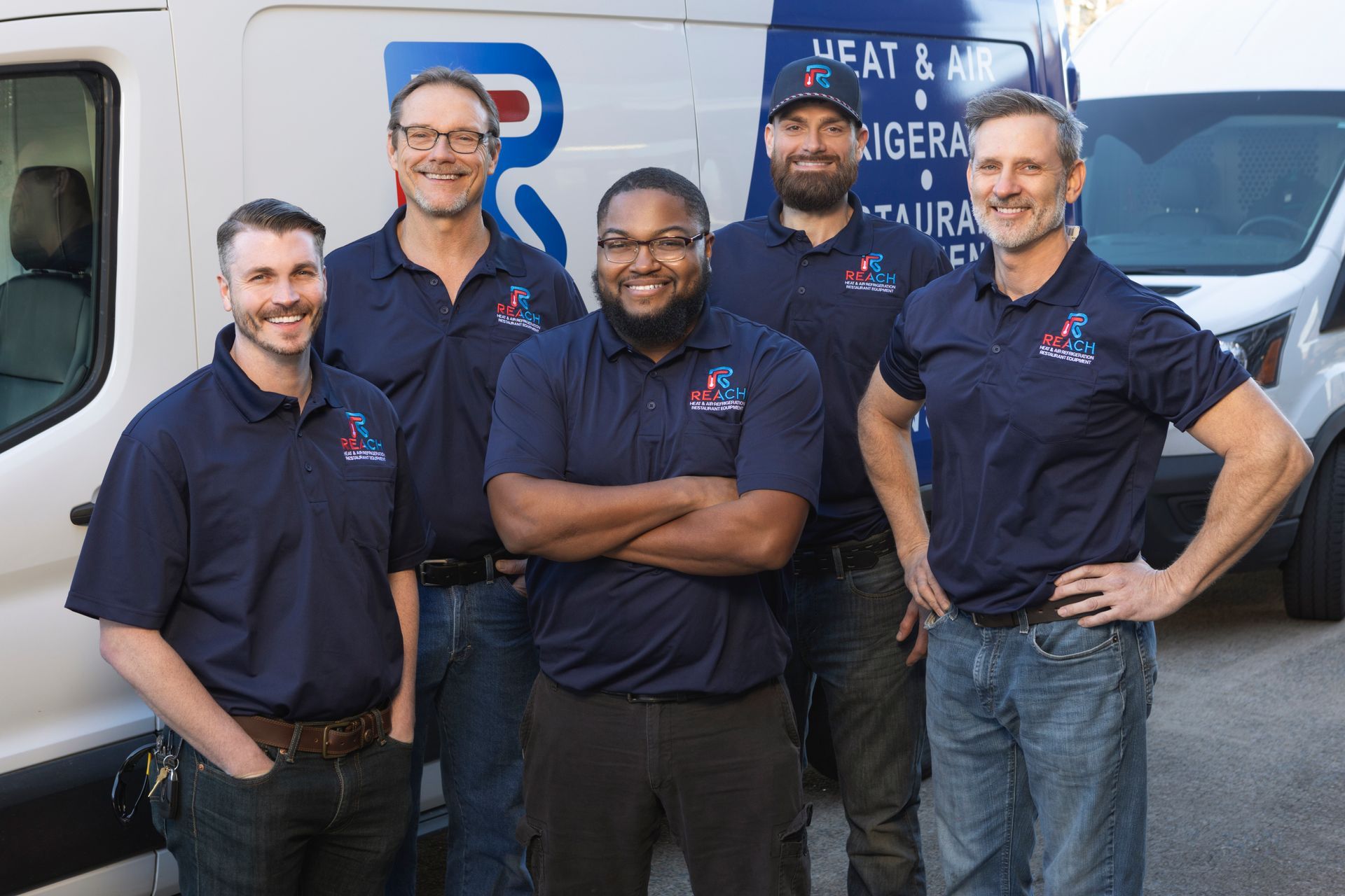 Five employees in matching dark blue company polo shirts stand smiling in front of a white work van.