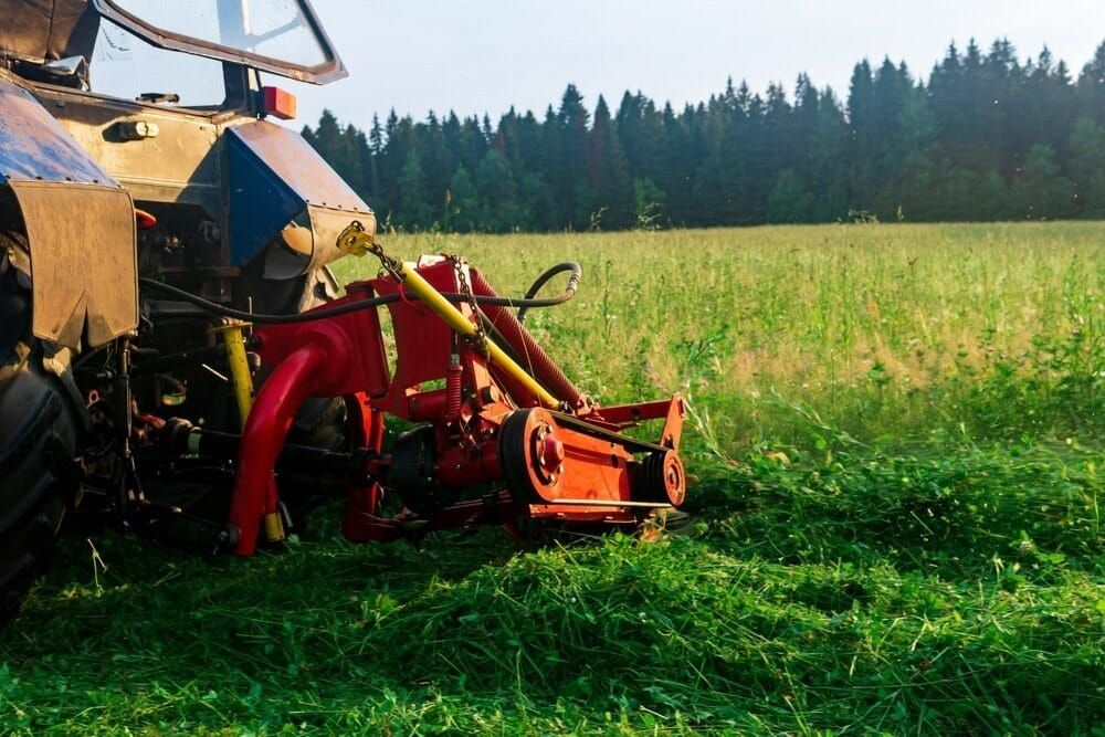 A Tractor Is Cutting Grass in A Field — Parkes Machinery Services PTY LTD in Parkes, NSW