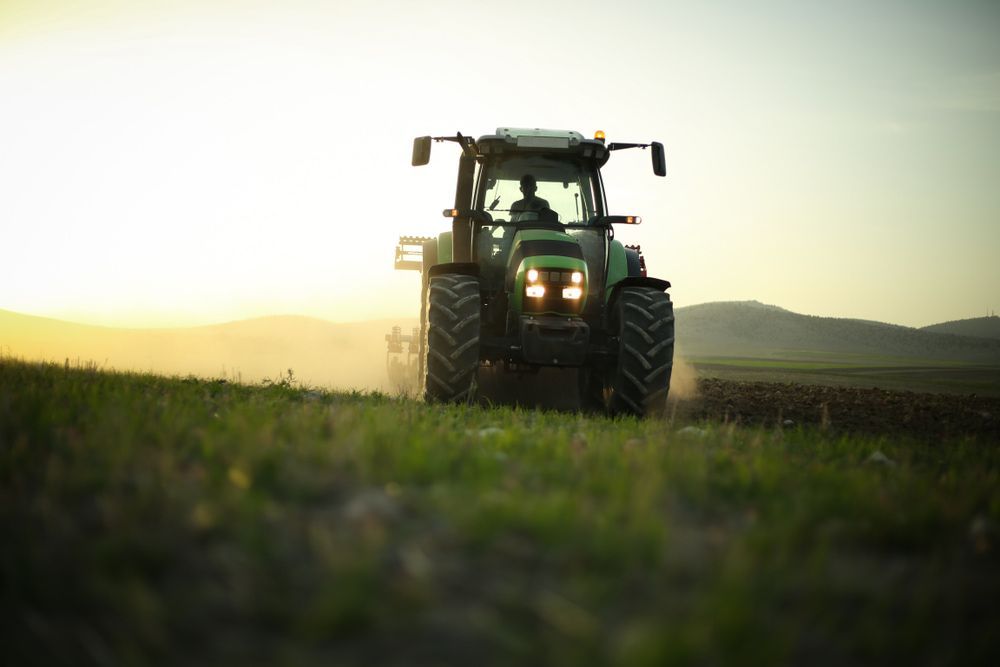 A Green Tractor Is Plowing a Field at Sunset — Parkes Machinery Services PTY LTD in Parkes, NSW