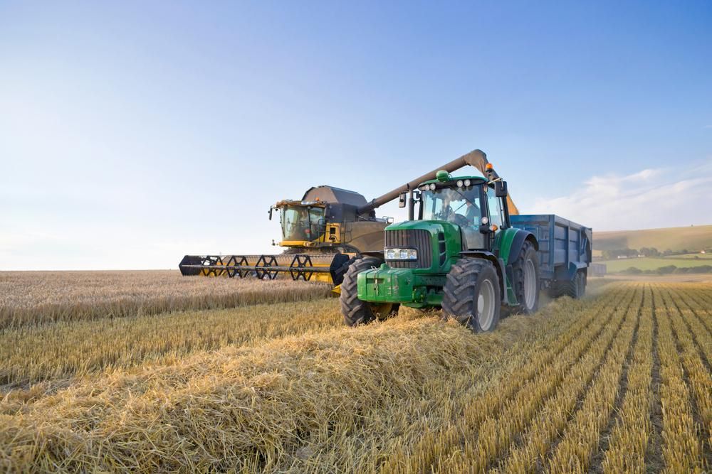 A Green Tractor Is Driving Through a Field Next to A Combine Harvester — Parkes Machinery Services PTY LTD in Parkes, NSW