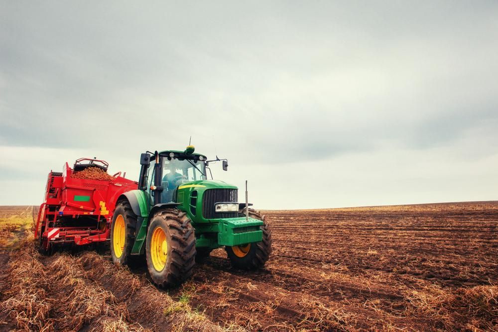 A Green and Red Tractor Is Plowing a Field — Parkes Machinery Services PTY LTD in Parkes, NSW