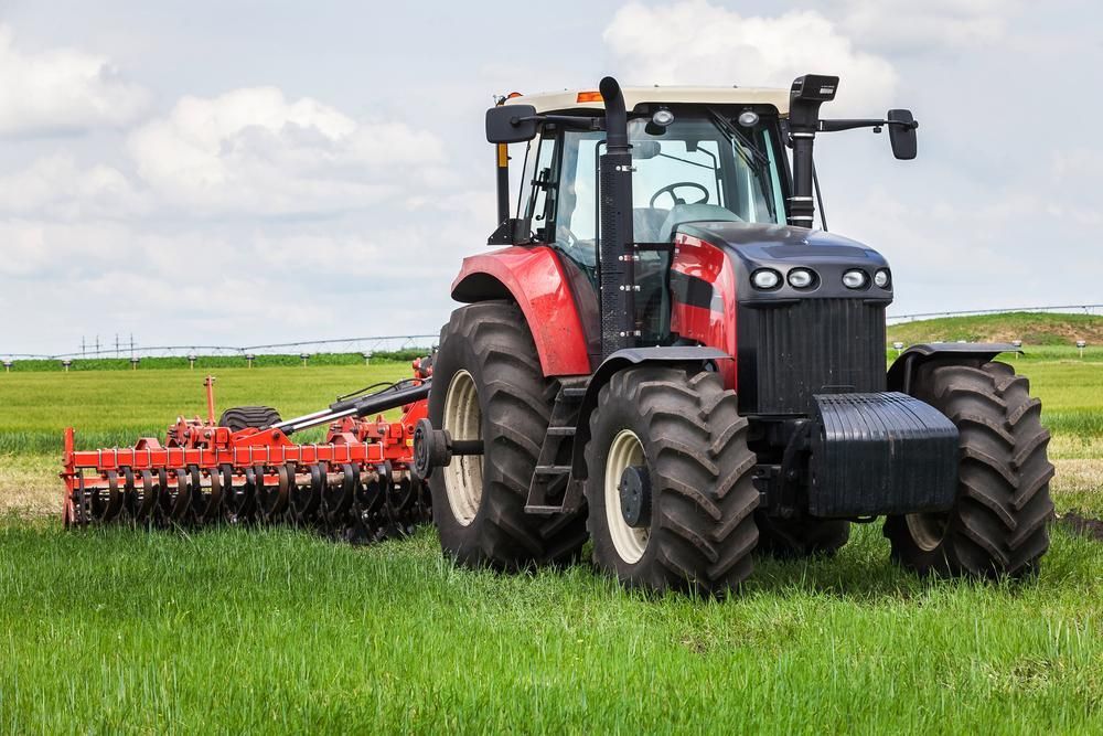 A Red Tractor Is Plowing a Field with A Plow Attached to It — Parkes Machinery Services PTY LTD in Nyngan, NSW